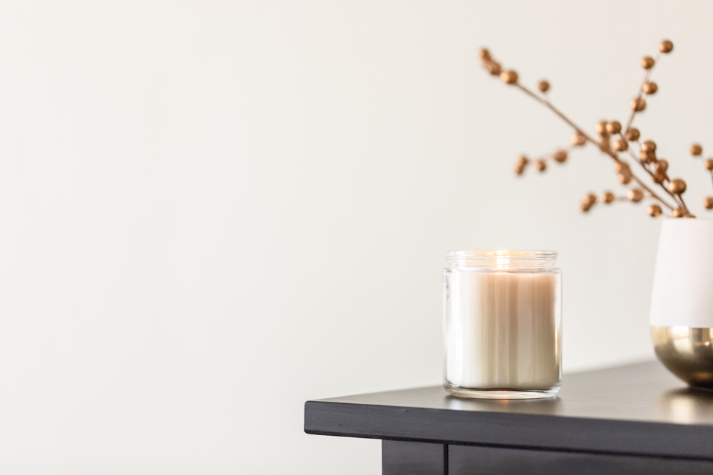 A candle in a glass jar and a vase with branches on a dark wooden table.